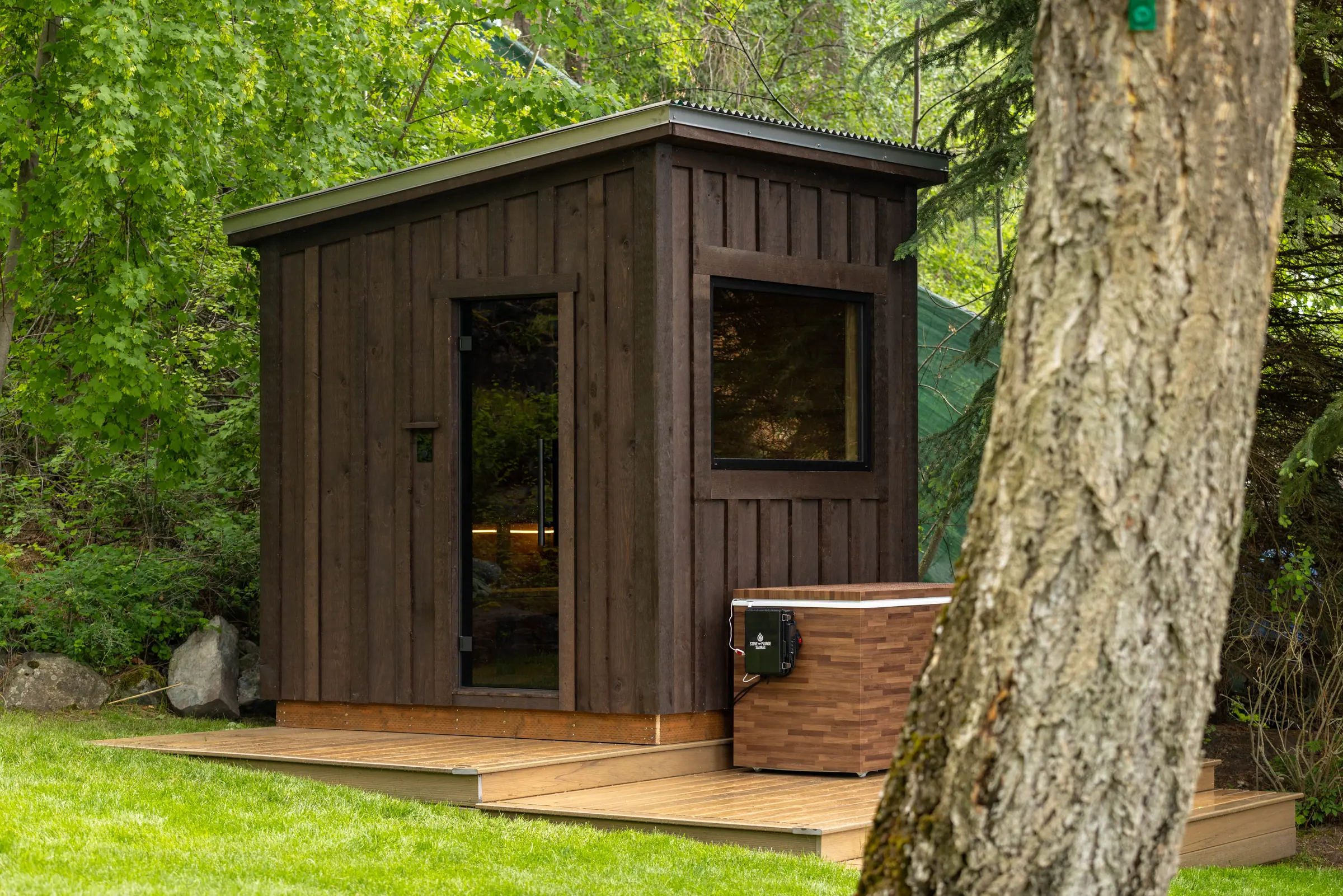 Dark-stained sauna on a cedar deck beside a cold plunge tub