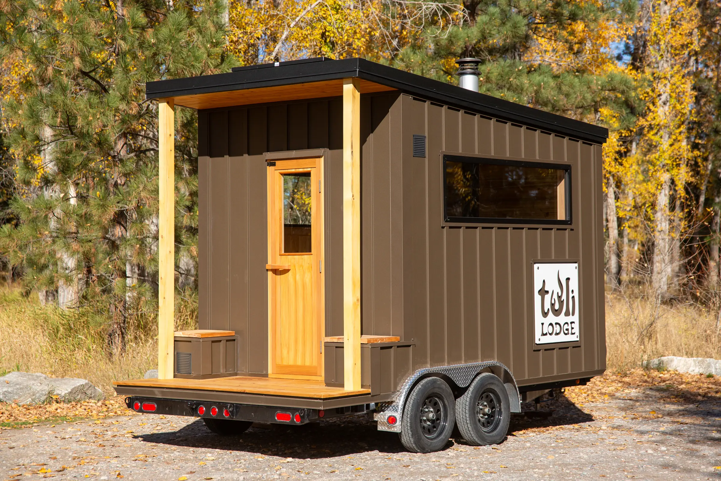 Mobile 10 sauna on its trailer with a cedar porch and door, autumn trees behind