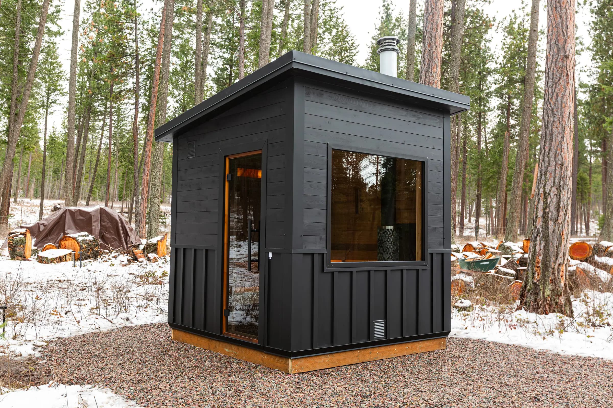 Black sauna with a large window in a snowy pine forest