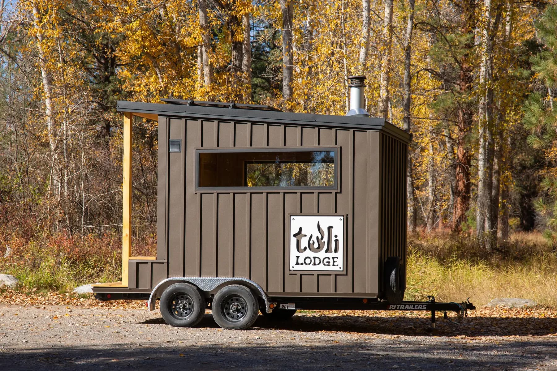 Mobile 10 sauna with dark vertical siding on a dual-axle trailer among autumn aspens