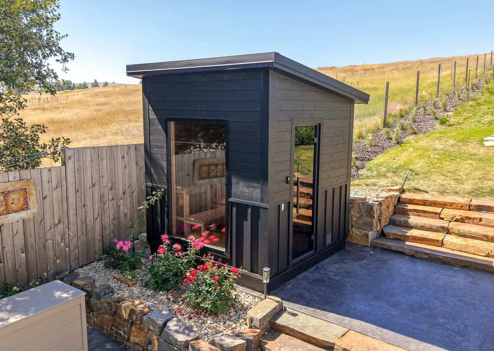 Brian Morgan’s black shed-roof sauna with a large window, beside rose beds and stone steps