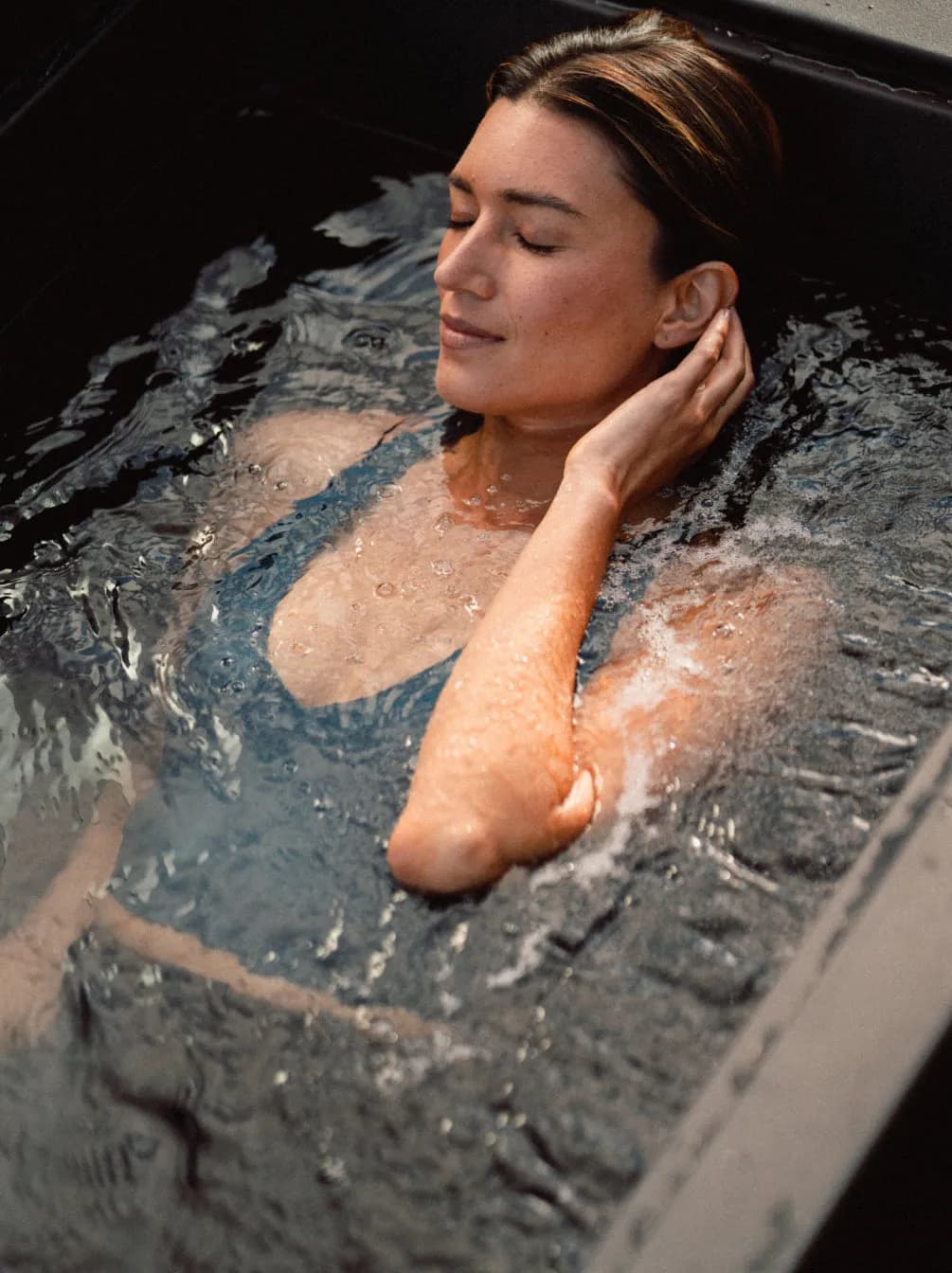 Woman sitting in clear, cold water in the plunge
