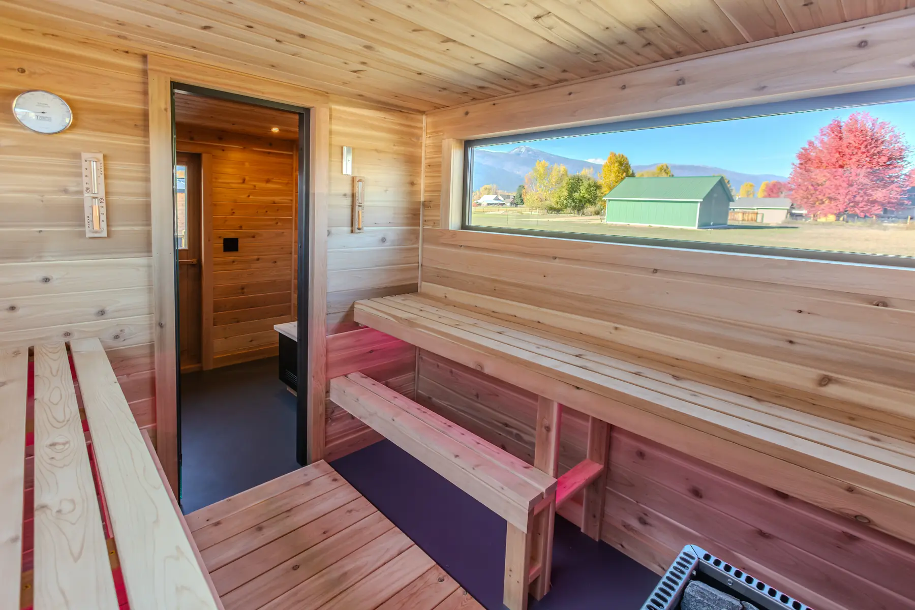 Mobile sauna interior with cedar benches, a long picture window and the door to the changing room