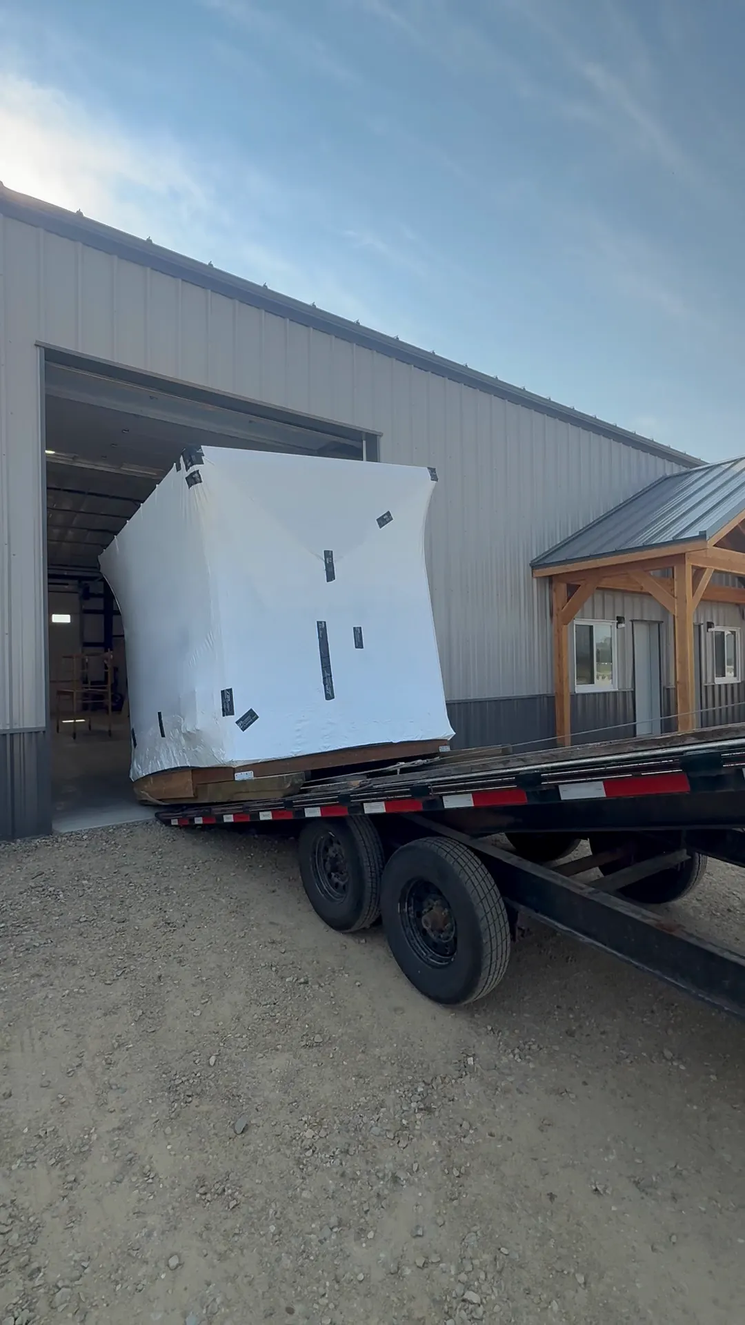 Wrapped sauna sliding onto a tilt trailer outside the shop