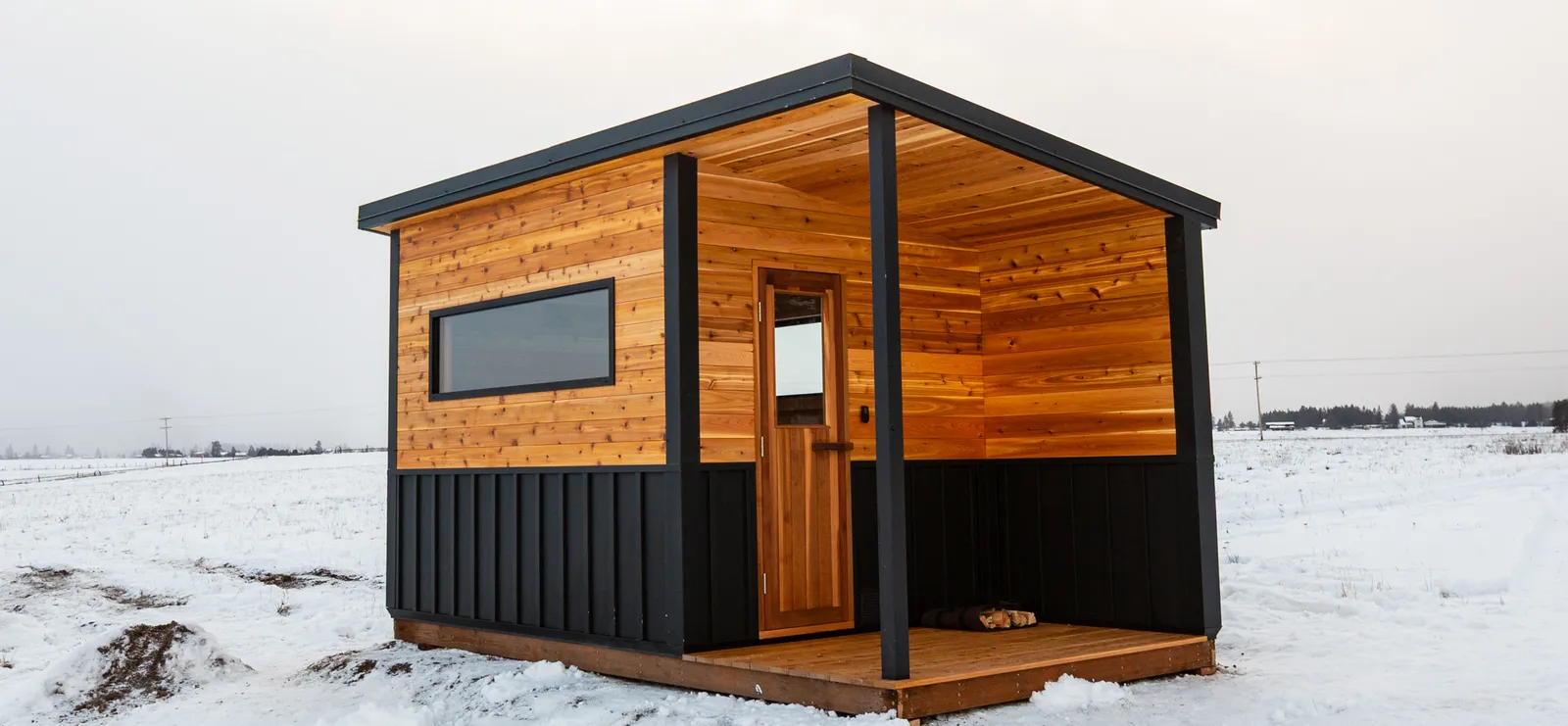 Model N sauna with cedar siding and a covered porch in an open snowy field