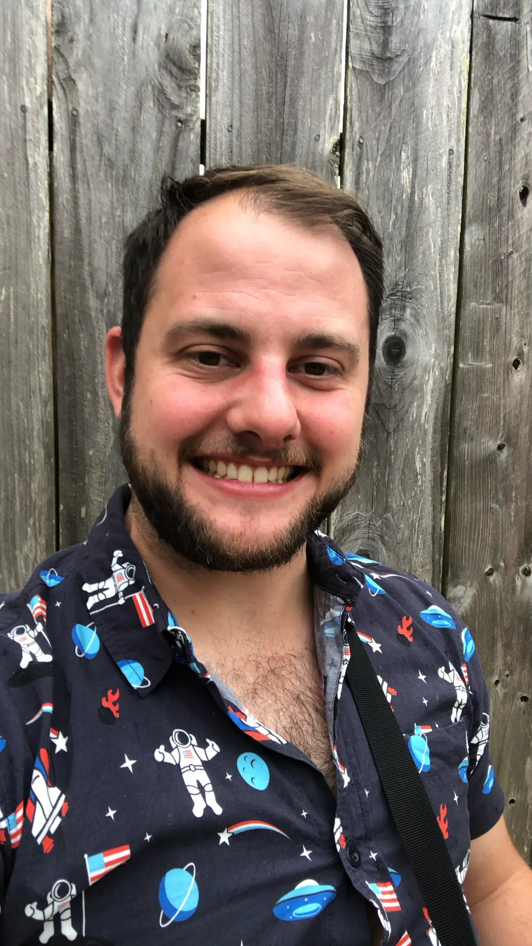 Paul Caso smiling in front of a weathered wood wall
