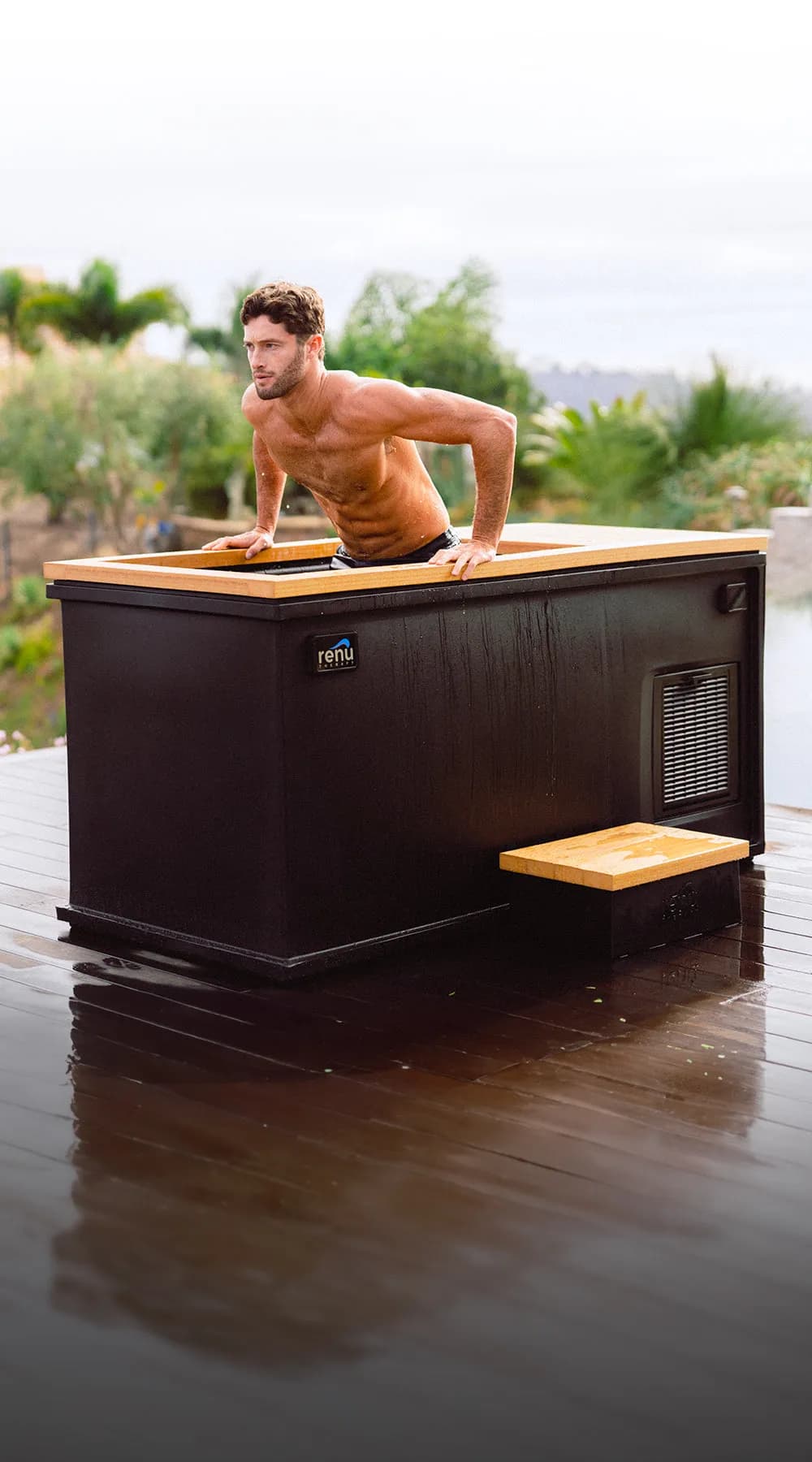 Man leaning on a black Cold Stoic 3.0 with a teak deck, beside an infinity pool