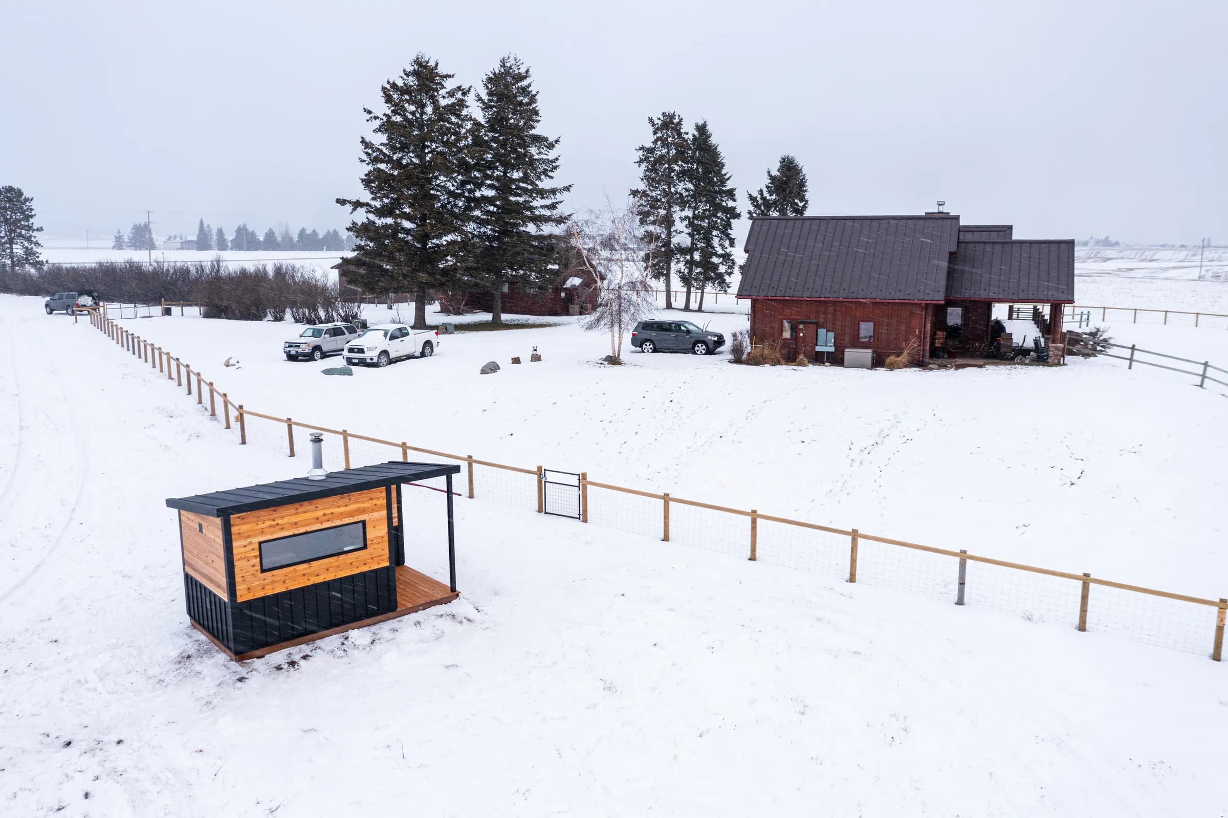 Model N in a snowy pasture below a ranch house and pines