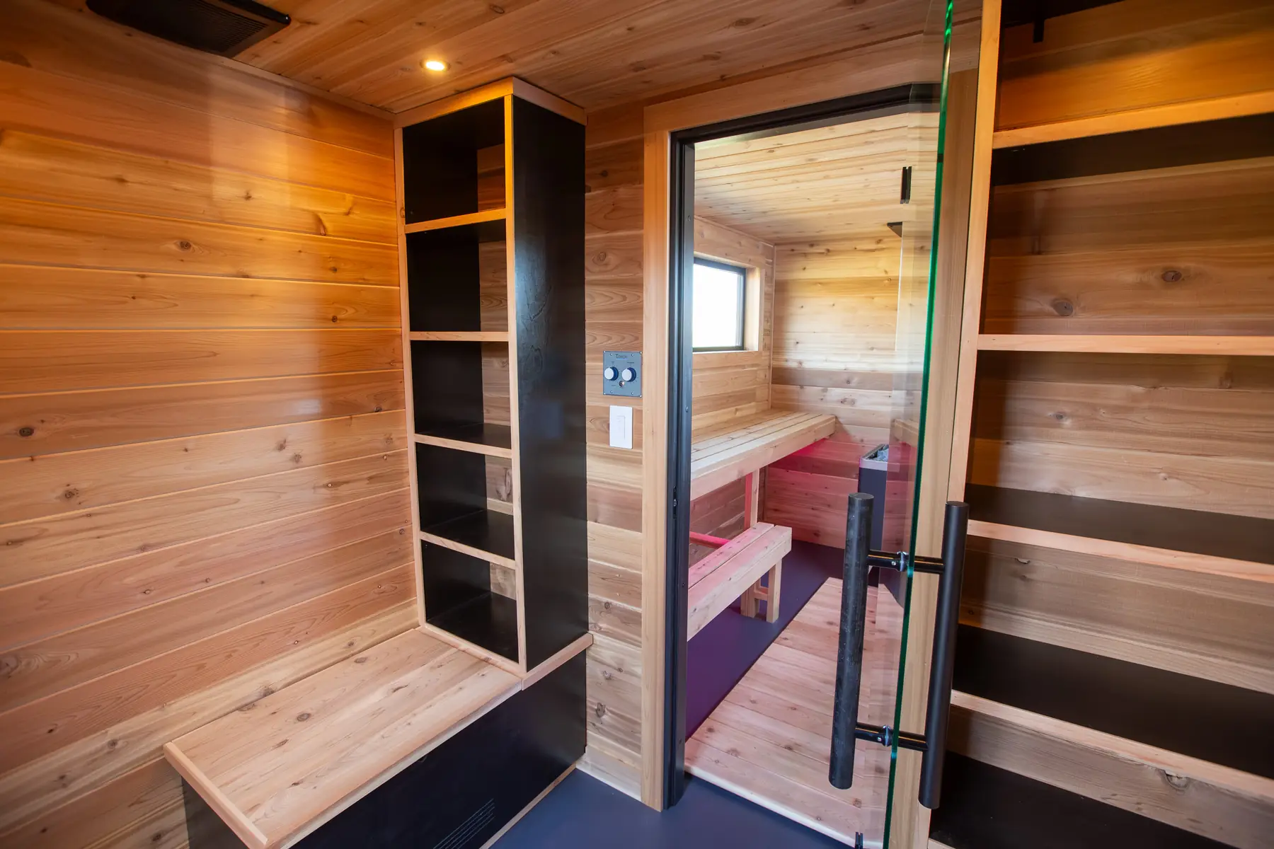 Cedar changing area with open shelves and a bench, the sauna door beyond