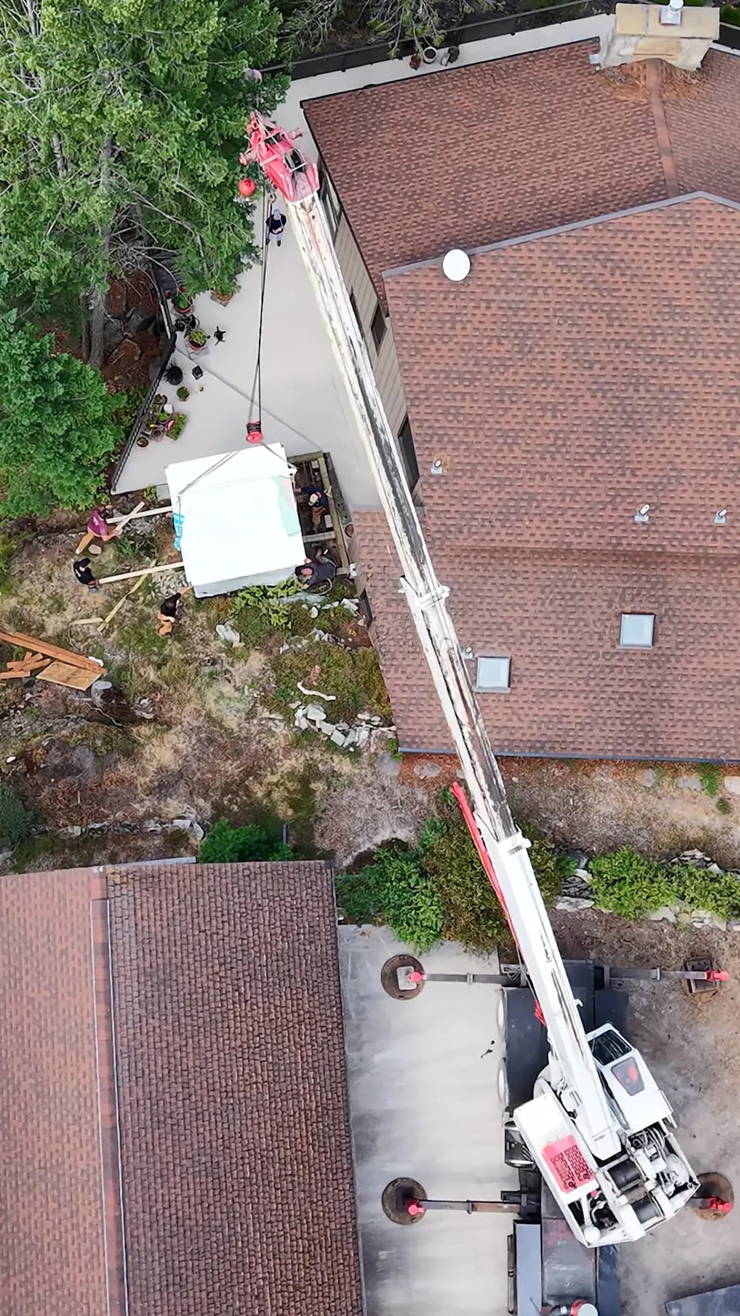 Aerial view of a crane setting a sauna beside a house