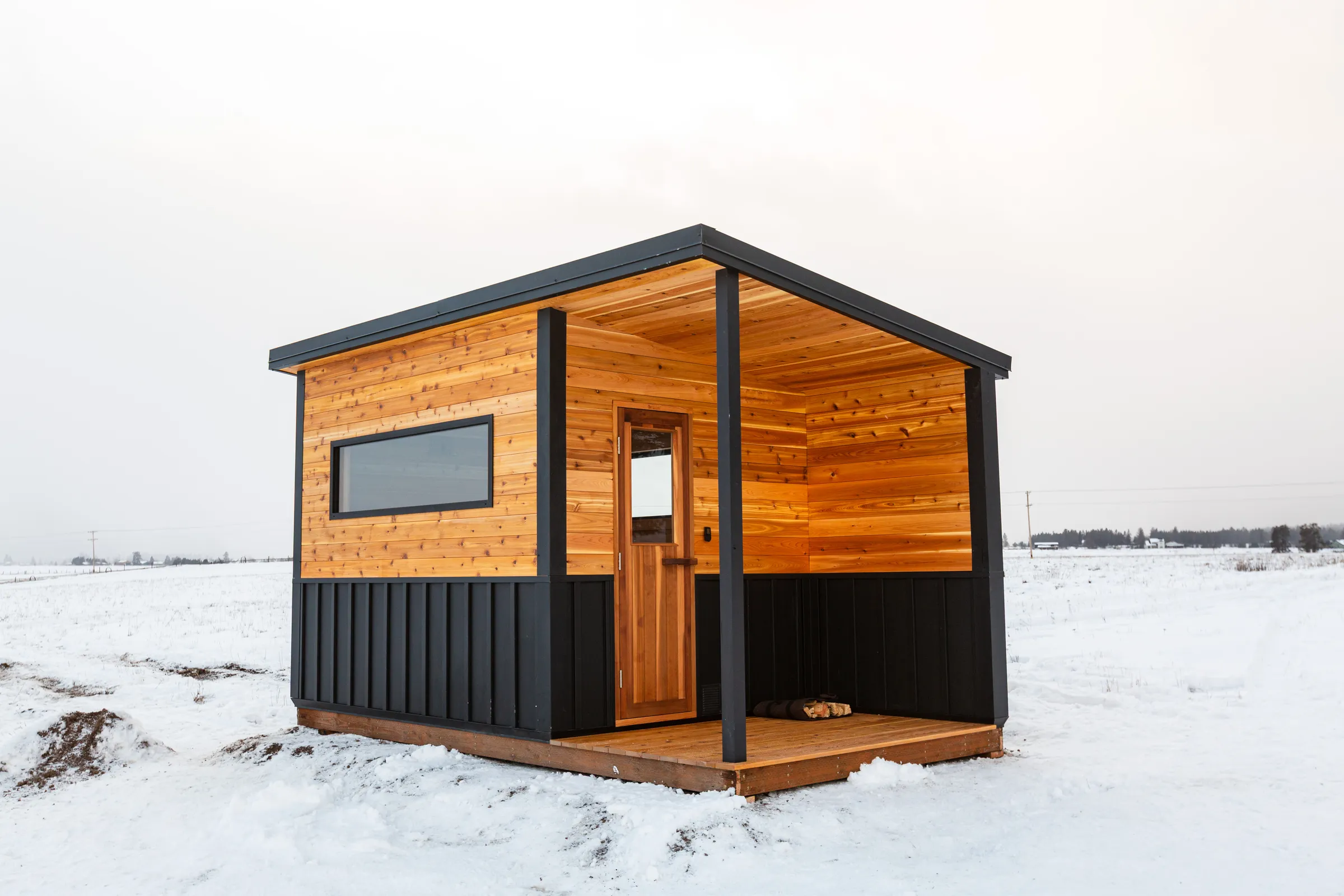 Model N with cedar siding, black lower walls and a covered porch on a snowy Kalispell field