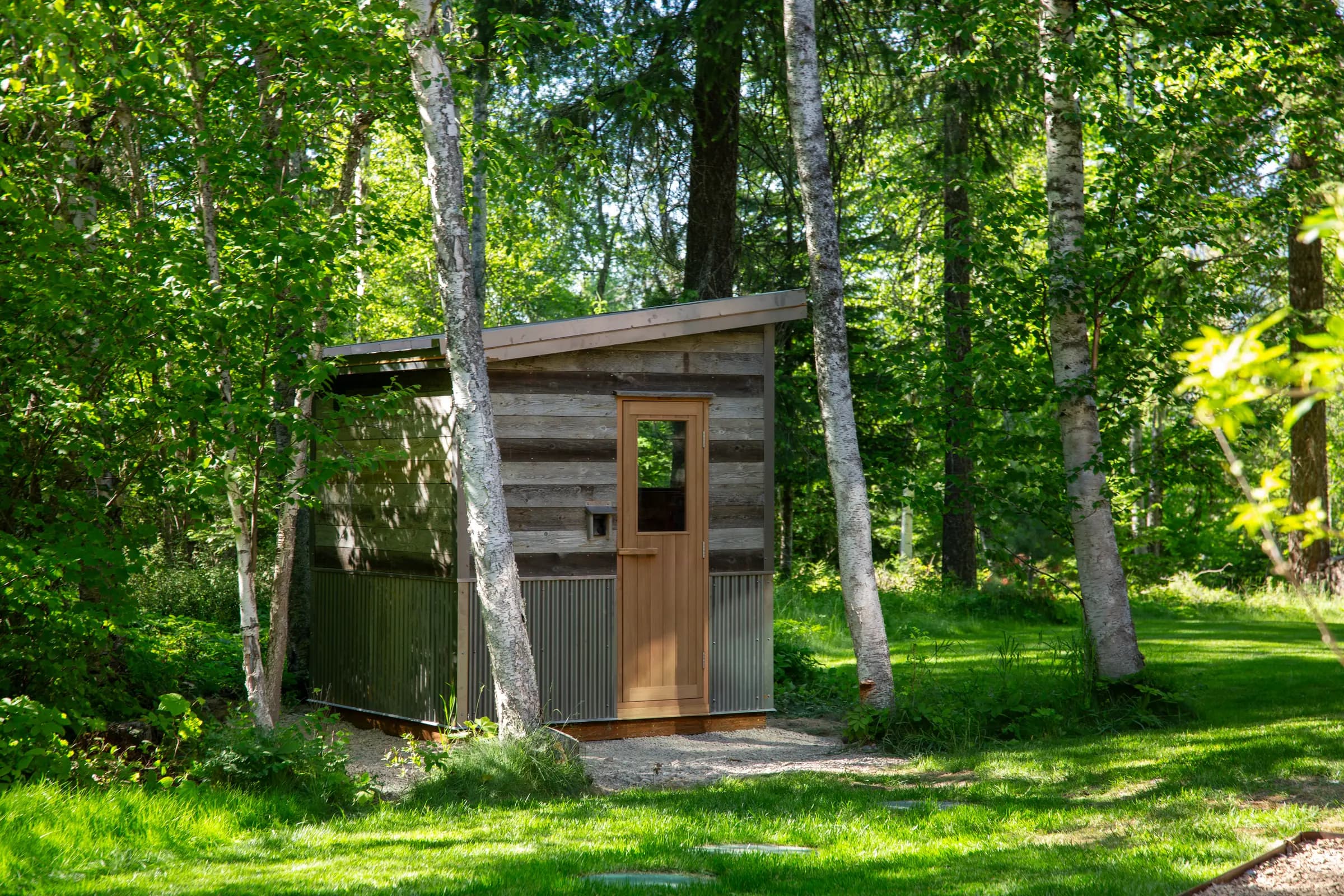 Reclaimed-wood sauna on a gravel pad at the edge of a lawn
