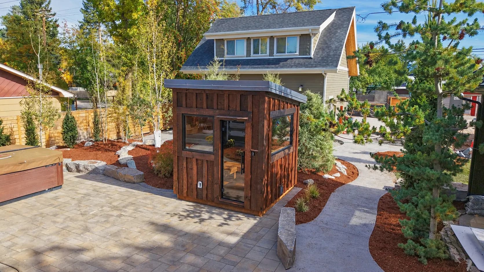 Dark-stained board-and-batten Model T with a glass door on a paver patio beside a hot tub