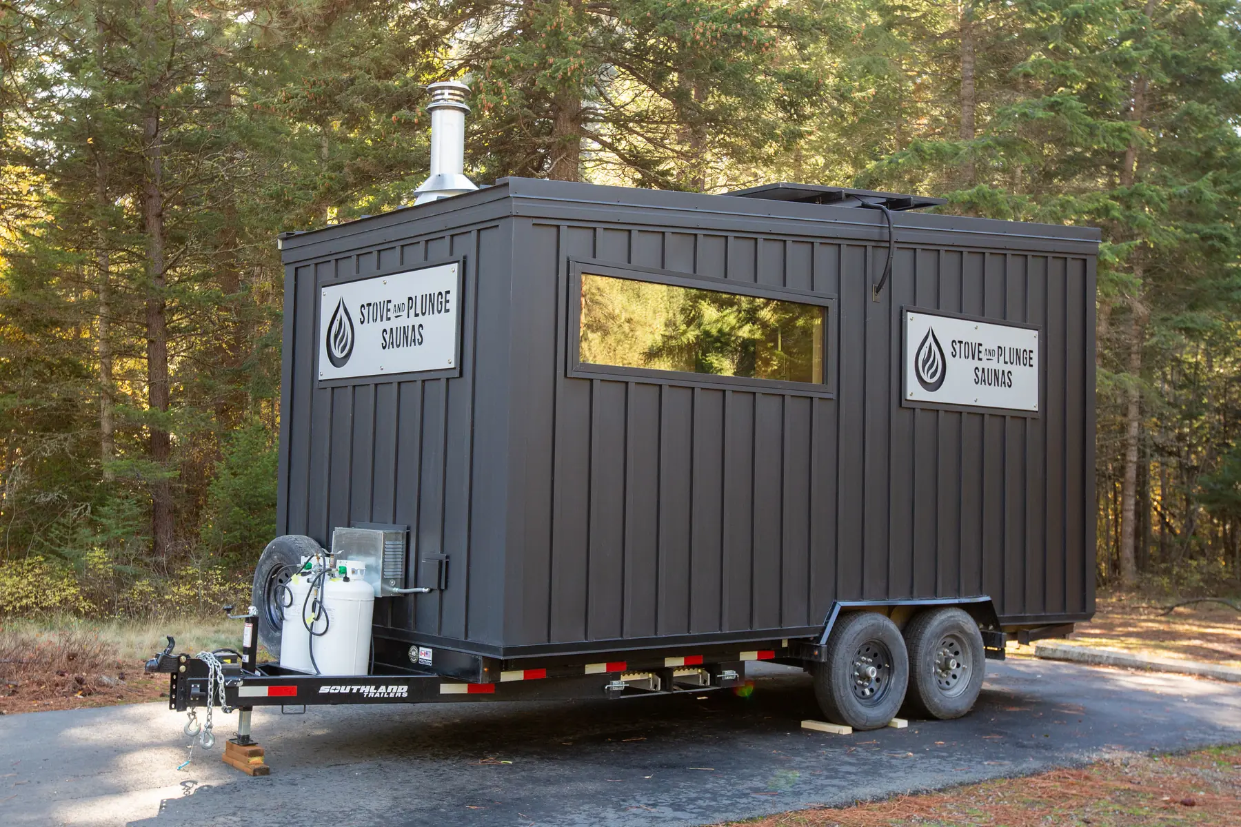 Mobile 10C with black vertical siding on a dual-axle trailer in a pine forest