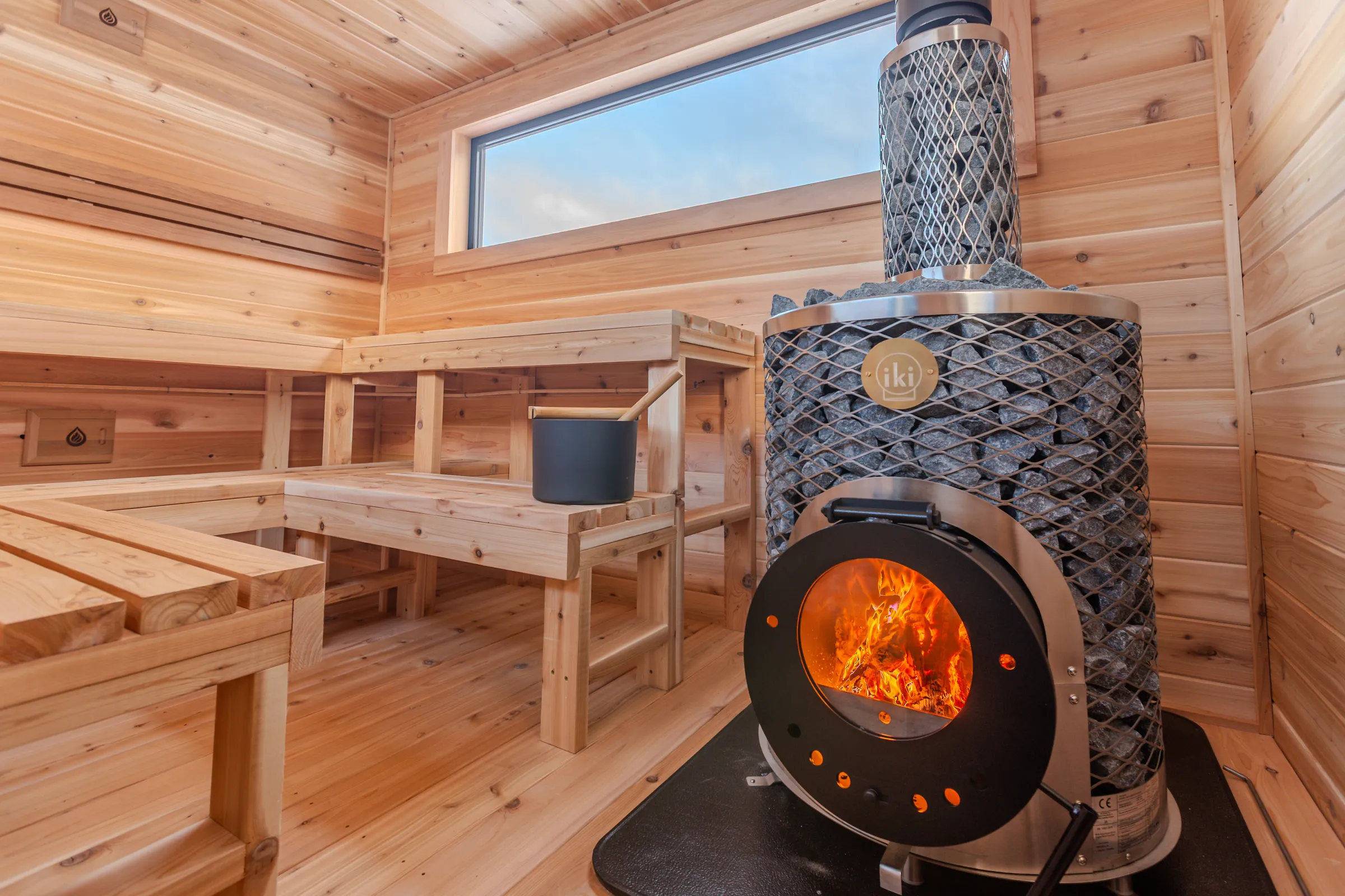 Fire in a wood-fired IKI stove beside cedar benches