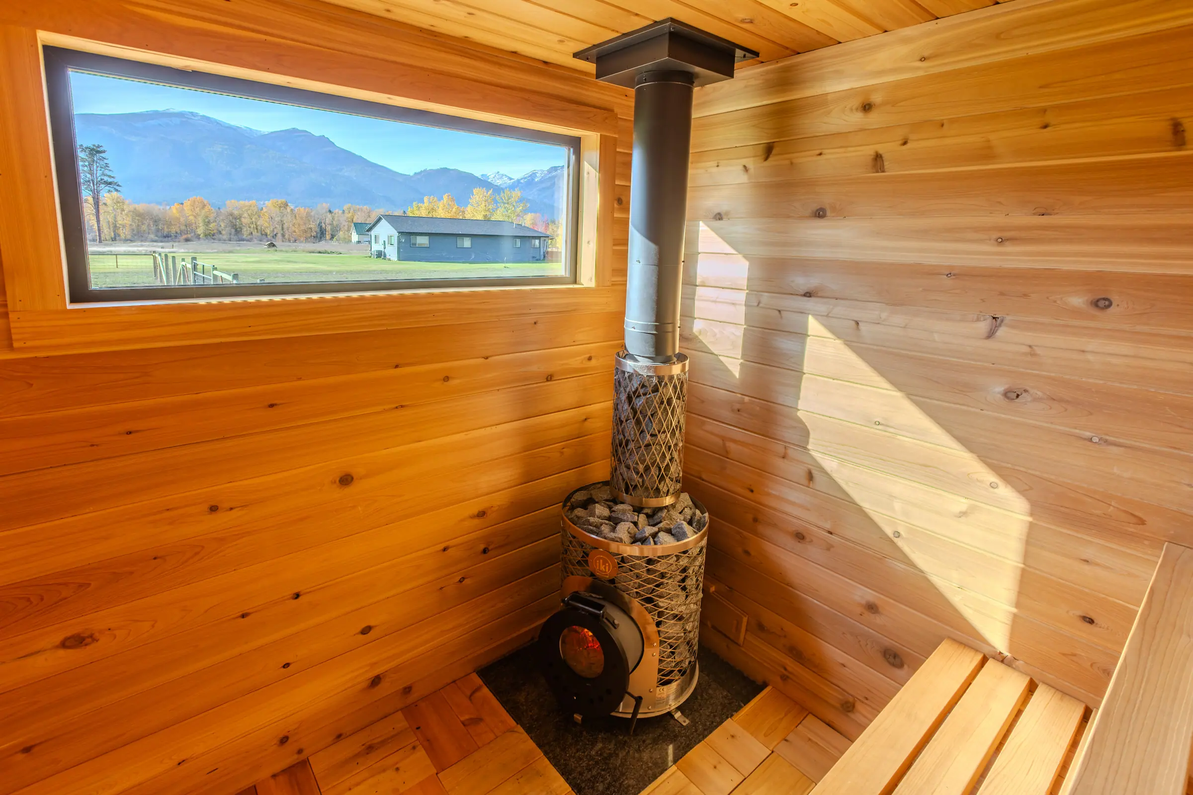 Wood-fired stove in a cedar corner beside a window onto mountains and autumn trees